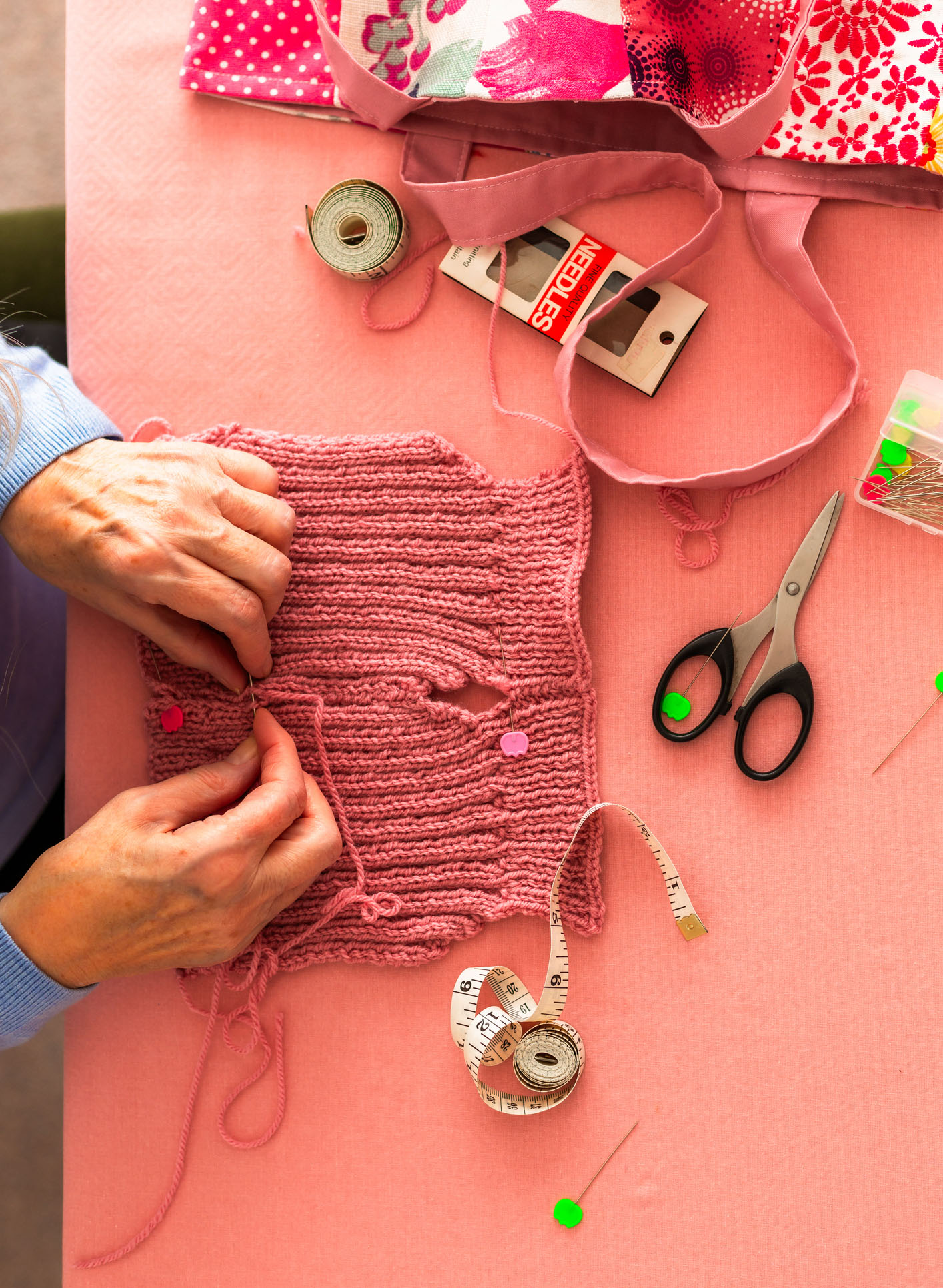 Hands of a senior woman knitting a pink woolen sweater.