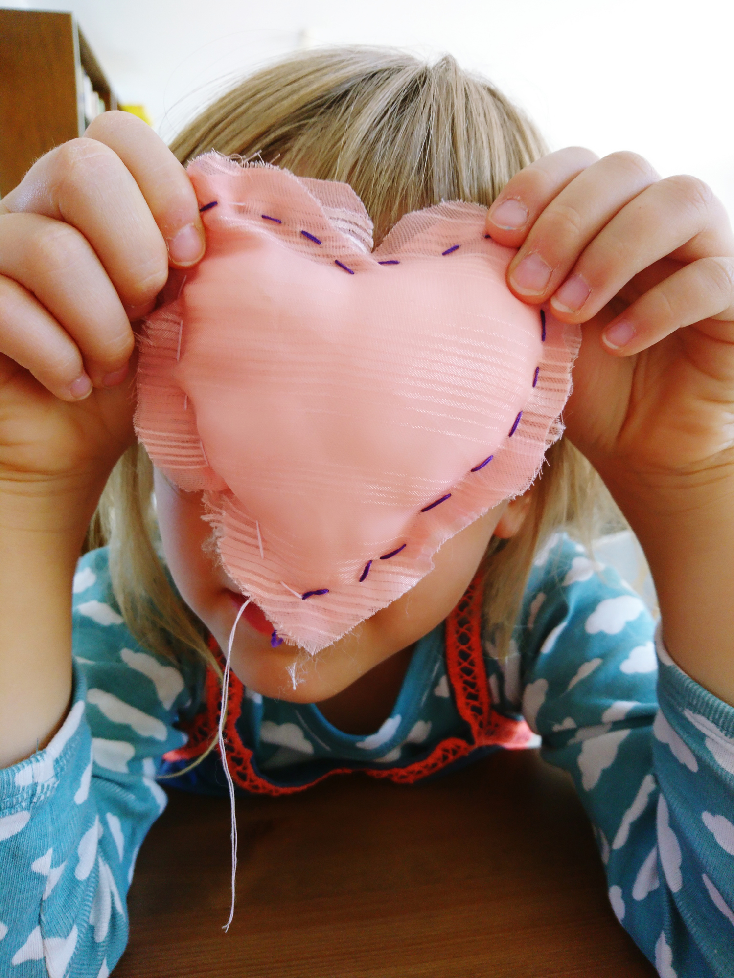 Young maker with a hand-stitched heart in front of their face.